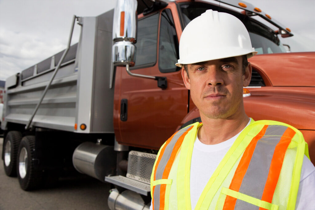 Dump Truck Driving Tips - Essential tips for dump truck drivers - Dump truck driver wearing safety hat in front of dump truck