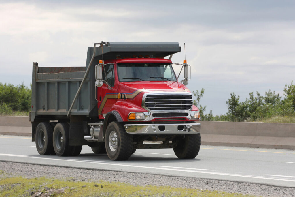 Guide to buying your first dump truck - red dump truck driving down road.