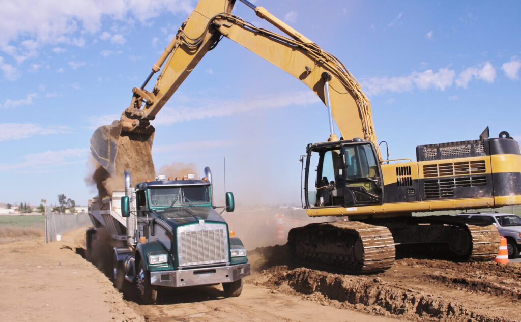 Dump truck market growth - Bottom dump truck being loaded by excavator