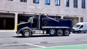 Blue dump truck on city street. Buy a Dump Truck New or Used Which Is Better