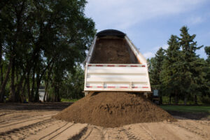 Dump truck unloading dirt pile outdoors. Title a Dump Truck